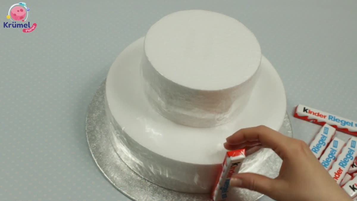 Candy Bar Cake basteln: Torte aus Schokoriegeln & Süßigkeiten - Kinderriegel grob an den vorbereiteten Klebestreifen befestigen.